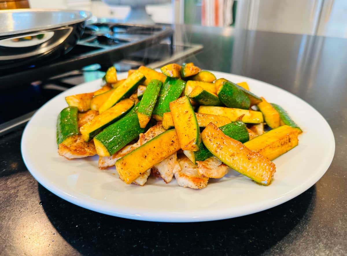 Cooked zucchini and chicken on a white plate.