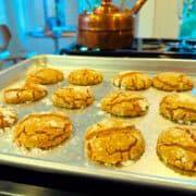 Molasses crinkle cookies on a baking sheet sitting on the stove next to a copper tea kettle.