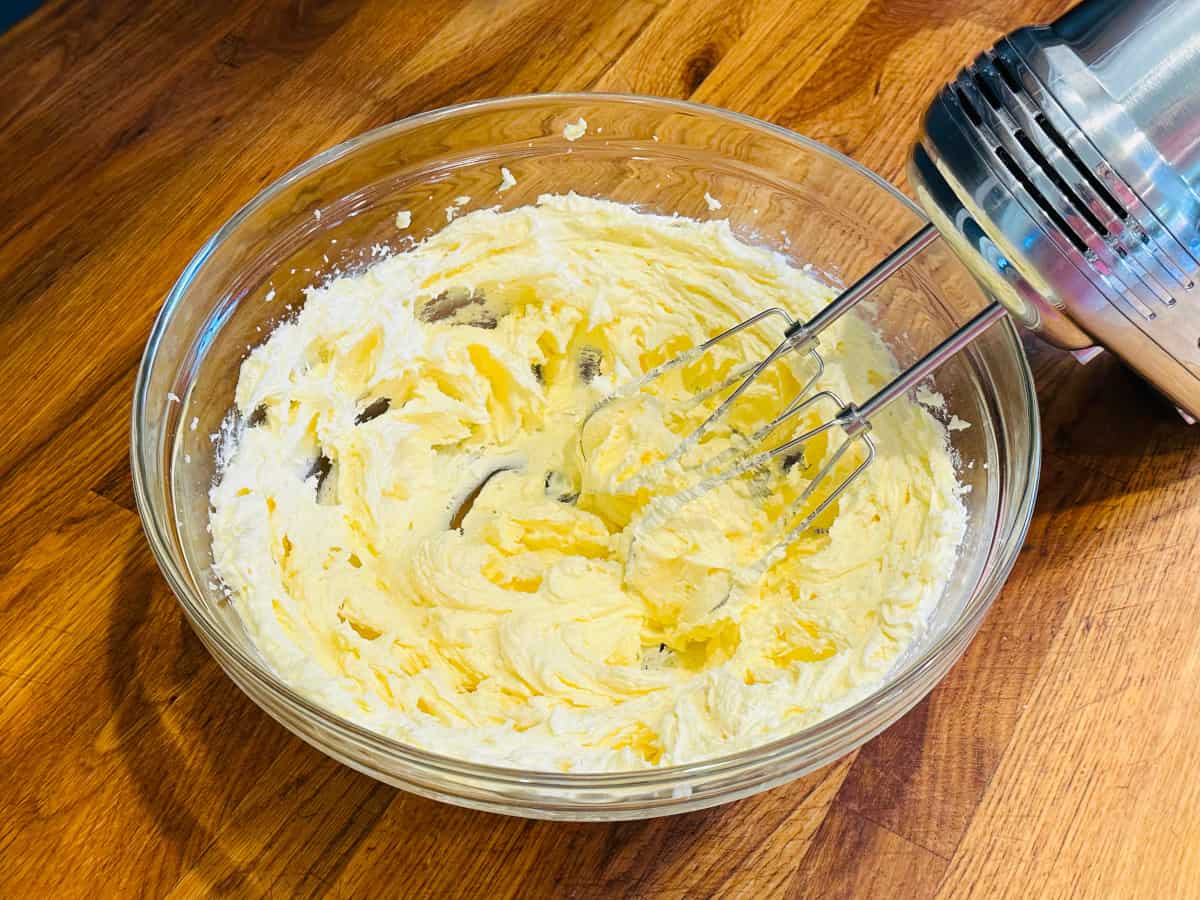Butter and sugar being creamed together in a glass bowl with an electric mixer.