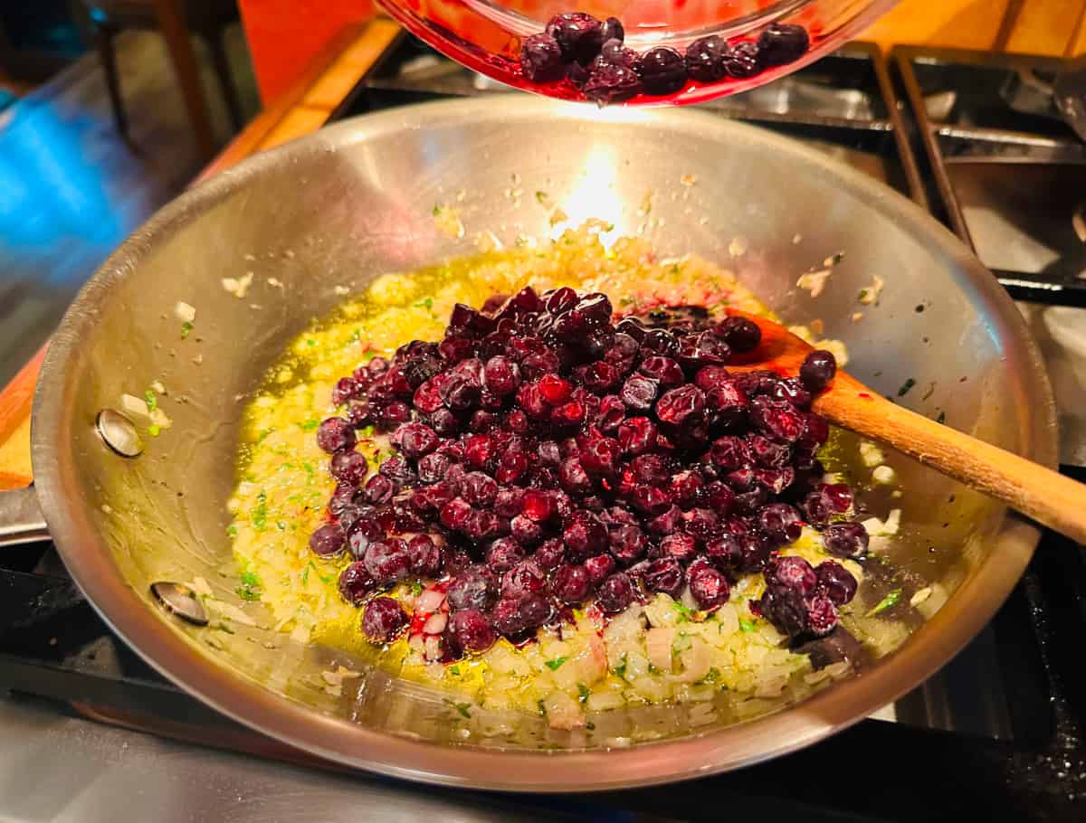 Blueberries being added to a steel skillet with chopped shallot and thyme.