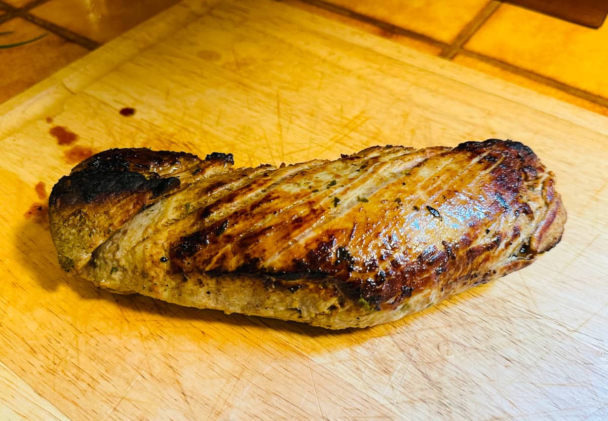 Roasted pork tenderloin resting on a wooden cutting board.