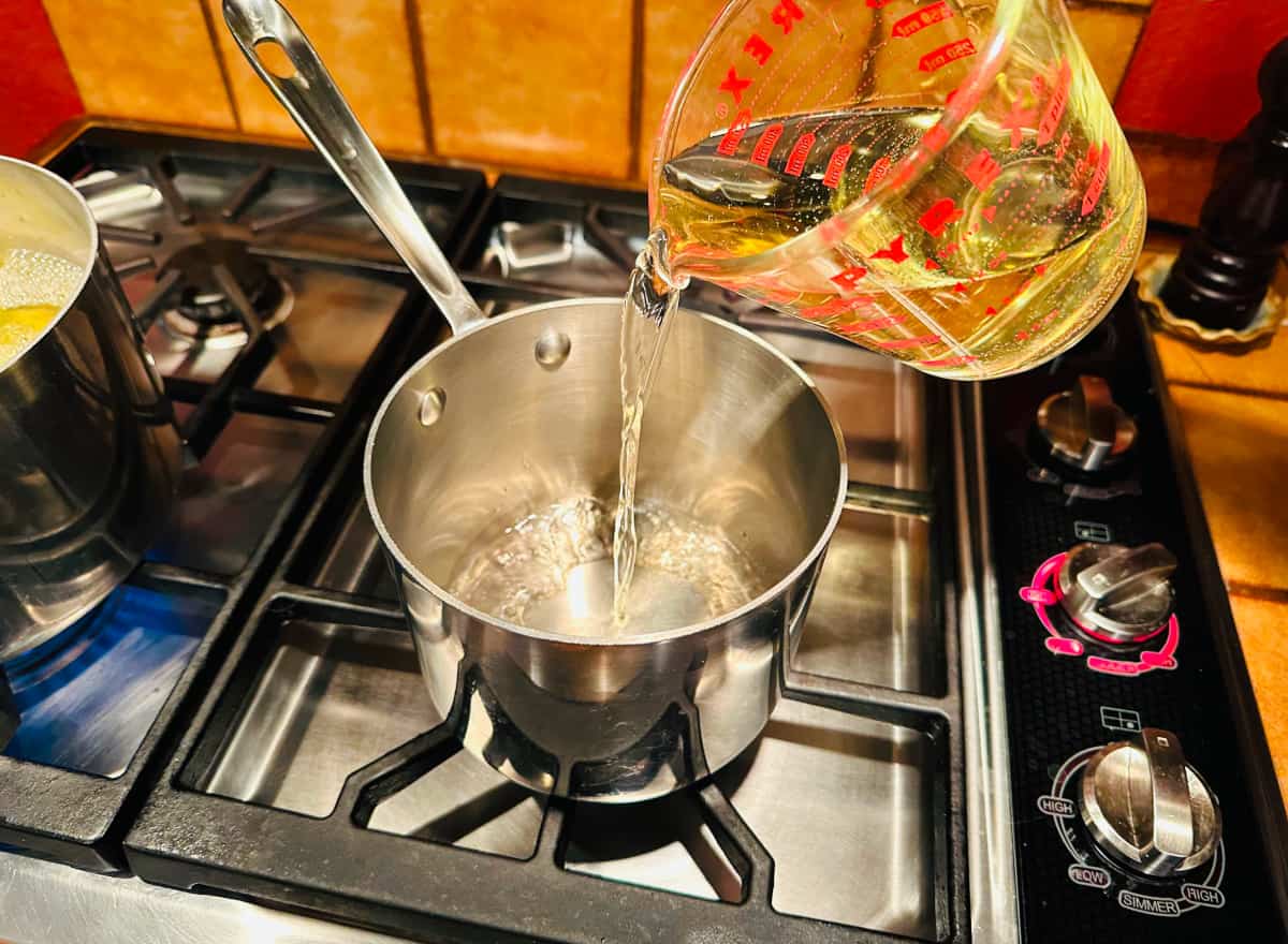 White wine being poured from a glass measuring cup into a small steel saucepan on the stove.