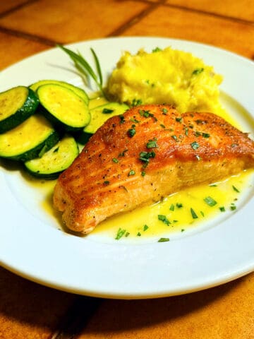 Tarragon salmon on a white plate with zucchini rounds and mashed potatoes.