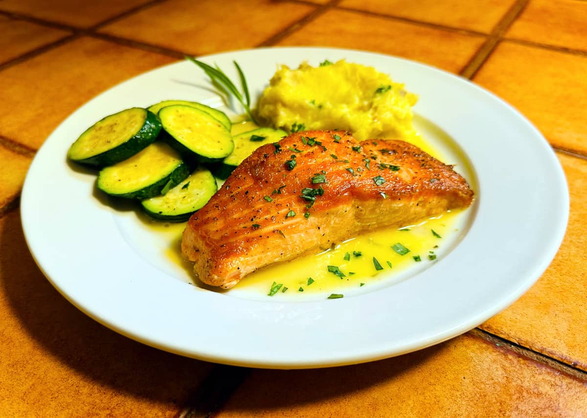 Tarragon salmon on a white plate with zucchini rounds and mashed potatoes.