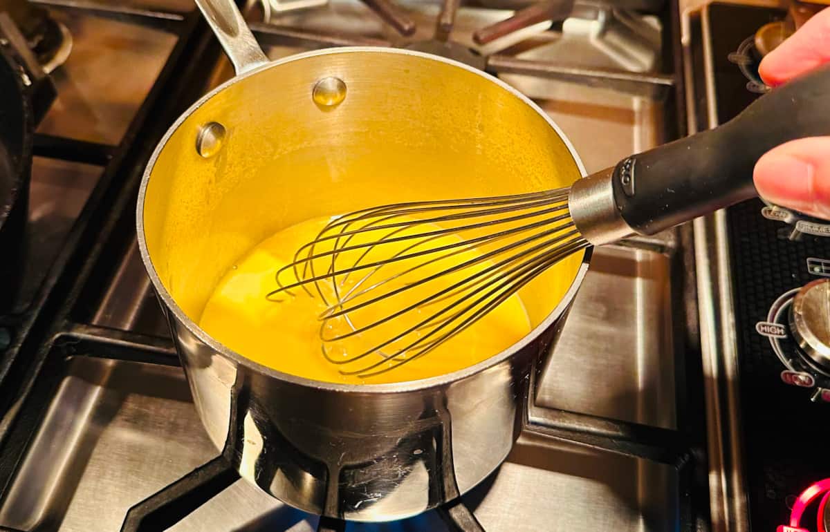 Butter cube being whisked into reduced wine in a small steel saucepan on the stove.
