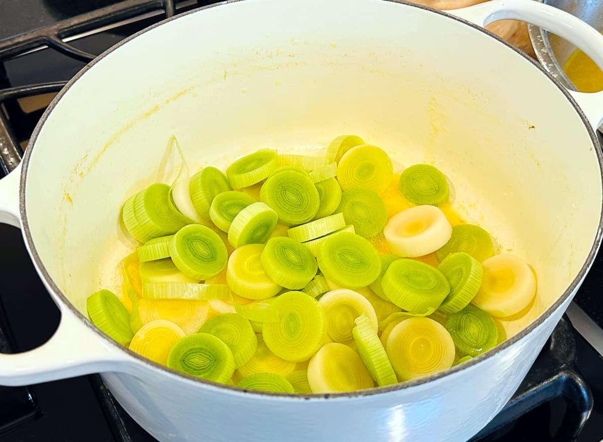 Thickly sliced leeks cooking in a large white pot.