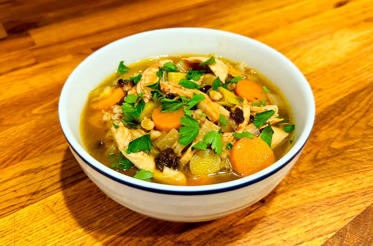 Cock-a-leekie soup in a white bowl with a navy stripe around the rim.