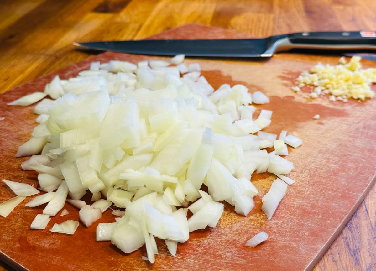 Chopped onions and minced garlic on a cutting board with a chef's knife.