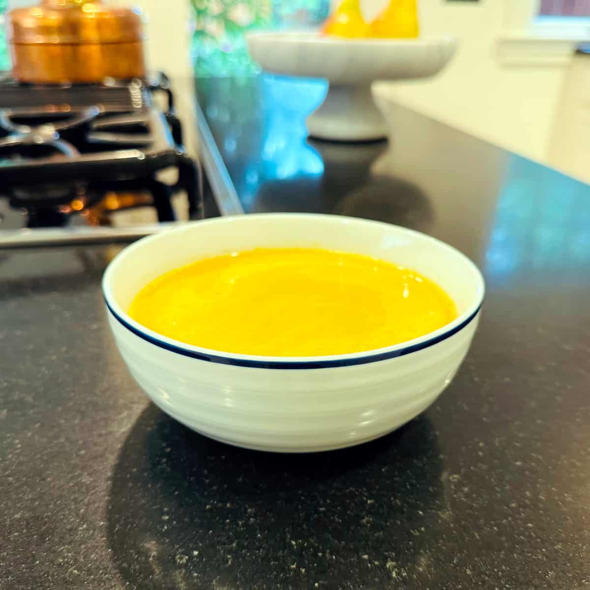 Curried pumpkin soup in a white bowl with a navy stripe around the edge.