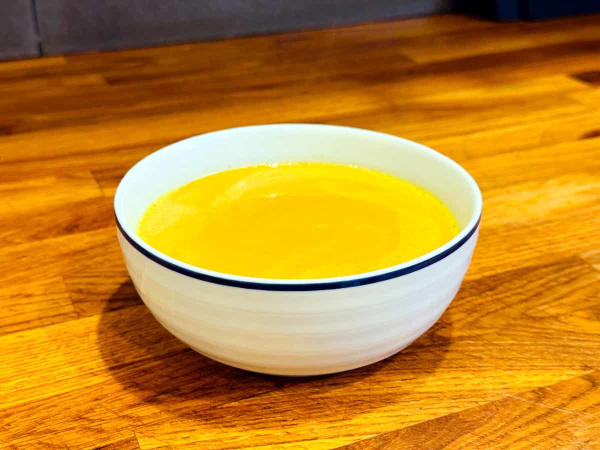 Curried pumpkin soup in a white bowl with a navy stripe around the edge.