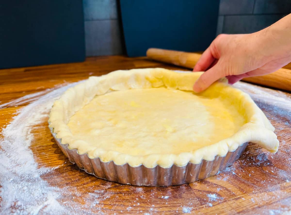 Excess crust dough being folded over into the sides of a tart pan lined with dough.