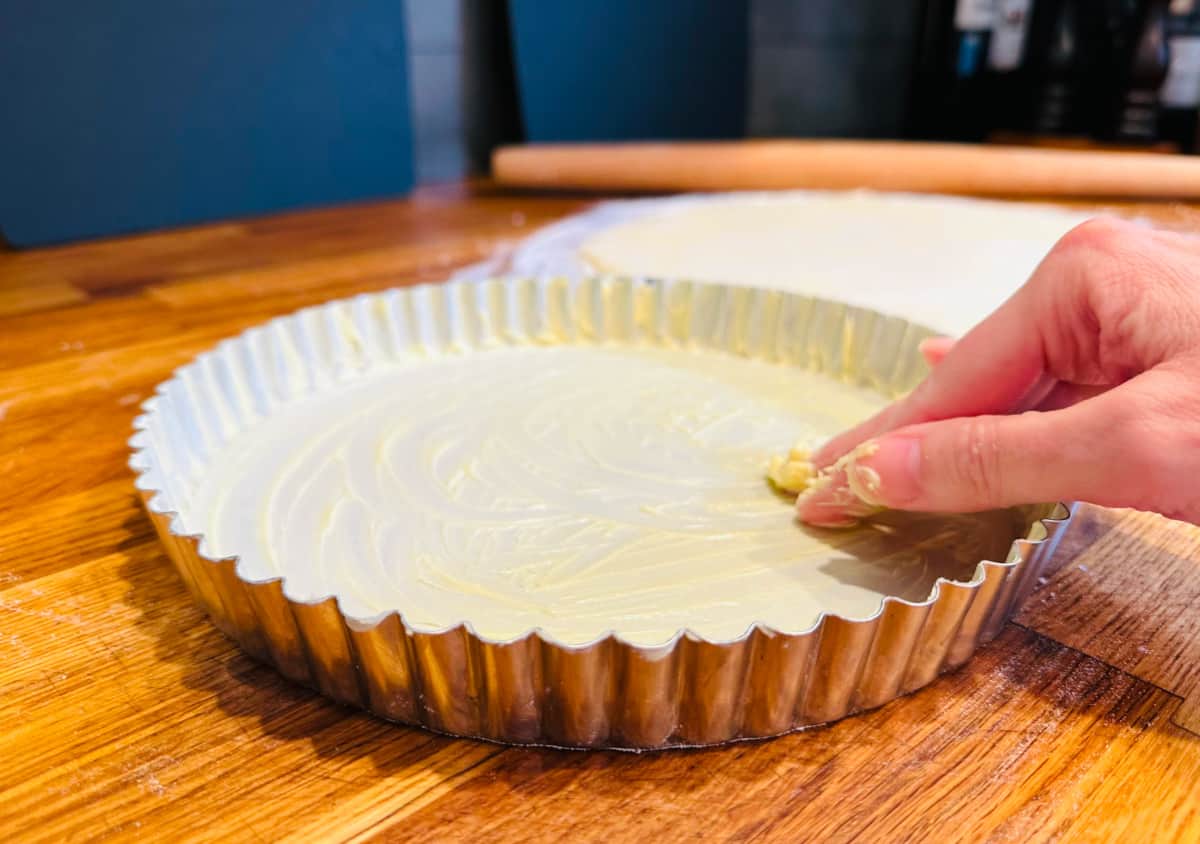 Tart pan being greased with fingers covered in butter.