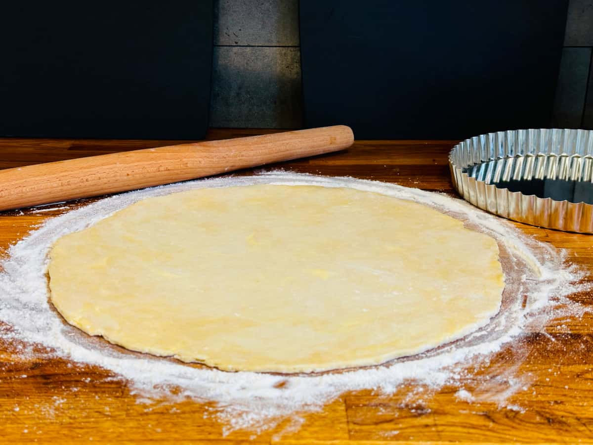 Butter pie crust dough rolled out into a large circle on a floured surface next to a rolling pin and tart pin.