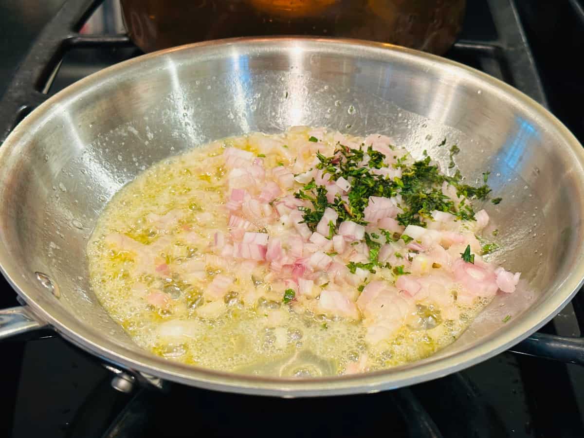 Chopped shallot and thyme cooking in butter in a small metal frying pan.