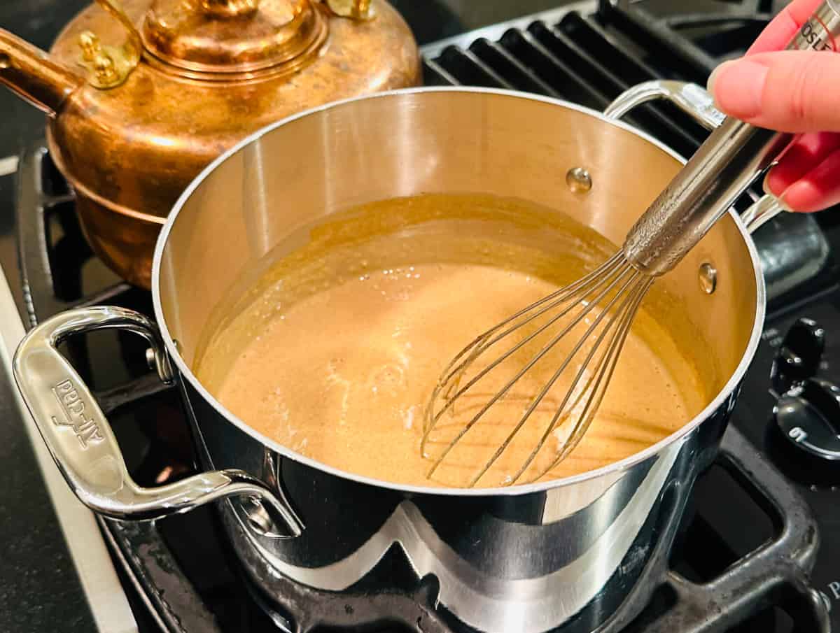 Bubbling light brown mixture being whisked in a steel saucepan on the stove.