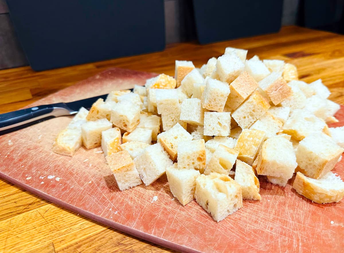 White bread cubes piled on a cutting board next to a knife.