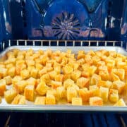 Homemade croutons roasting on a metal baking sheet in a blue oven.