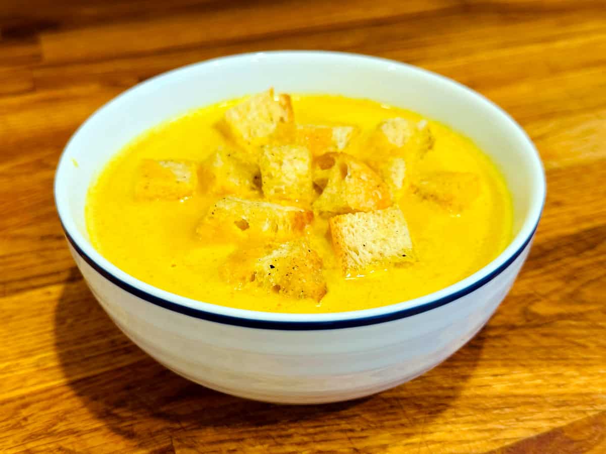 Curried pumpkin soup topped with croutons in a white bowl with a blue stripe around the edge.