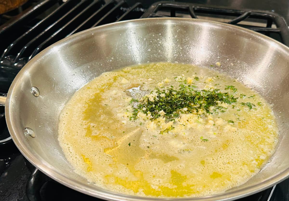 Minced thyme and garlic cooking in melted butter in a large steel skillet.