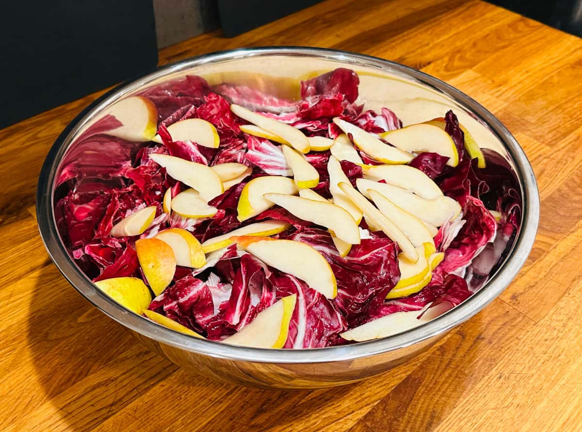 Torn radicchio leaves and sliced pears in a large metal bowl.