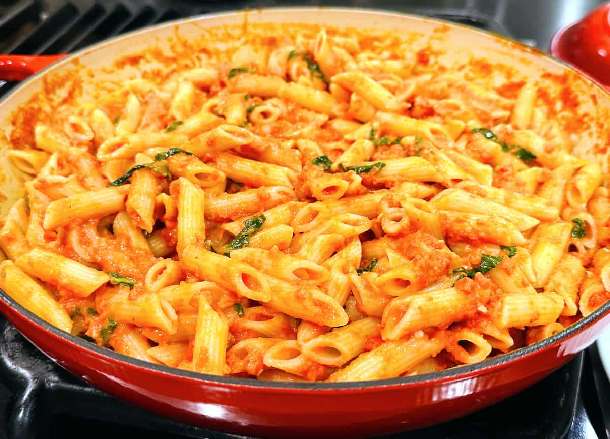Penne with tomato cream sauce in a large red braiser.