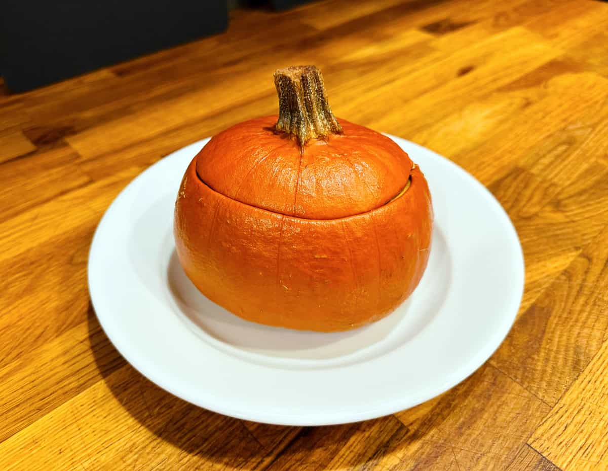 Pumpkin stuffed with everything good with lid on a white plate.