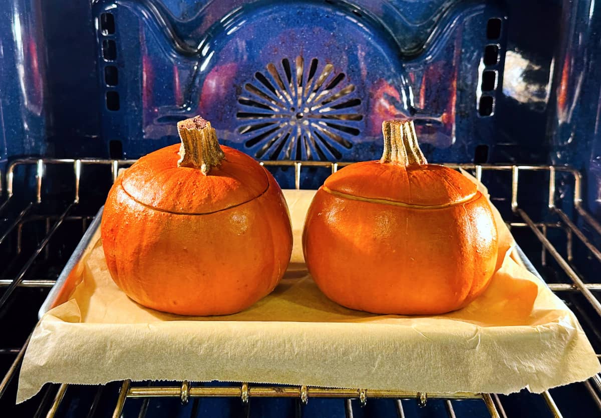 Two small pumpkins roasting on a parchment covered baking sheet in a blue oven.