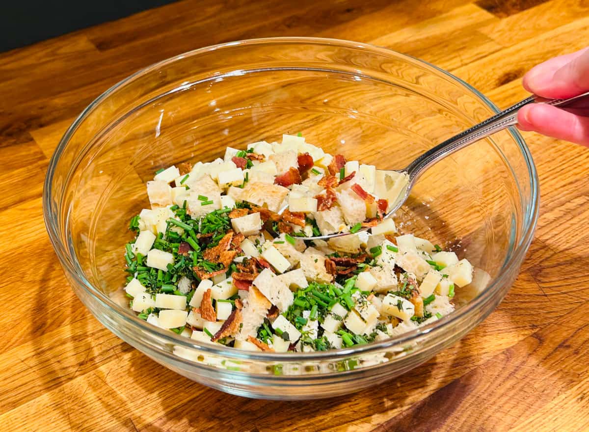 Stuffing ingredients being tossed in a glass bowl with a metal spoon.