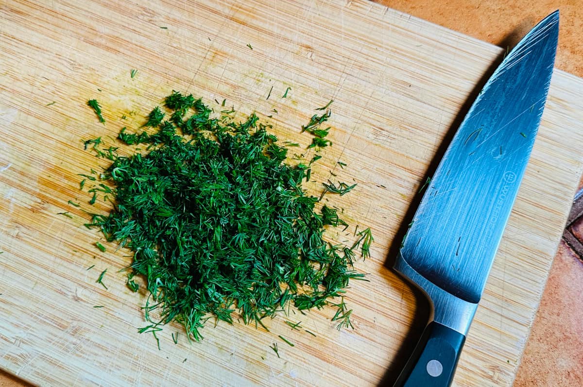 Chopped dill on a cutting board next to a chef's knife.
