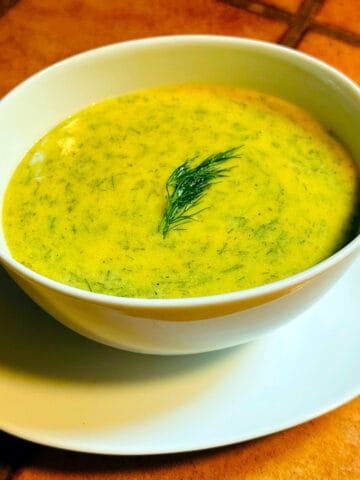 Scandinavian mustard dill sauce garnished with a sprig of dill in a white serving dish sitting on a terra cotta tile countertop.