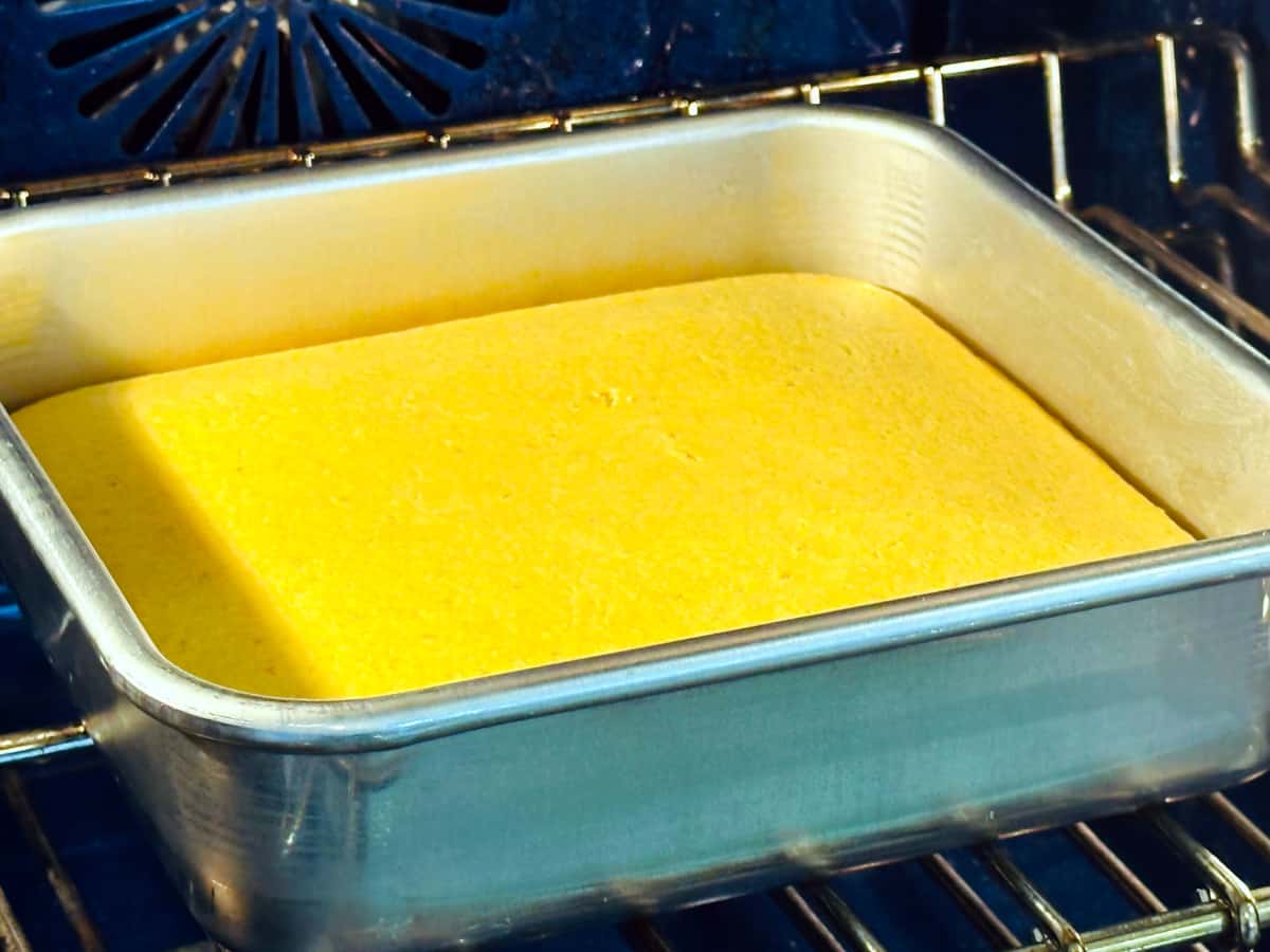 Cornbread in a square metal pan baking in the oven.