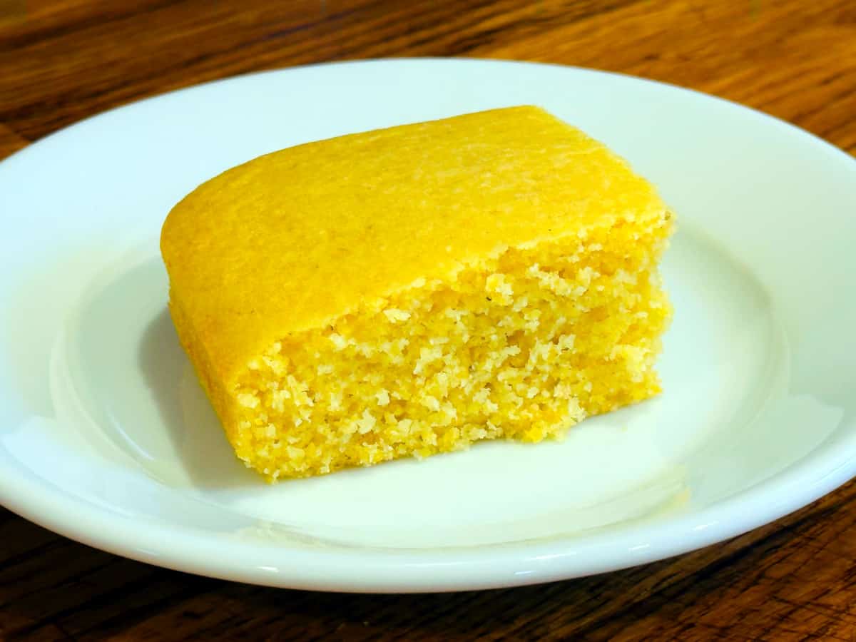 Slice of yellow cornbread on a small white plate.