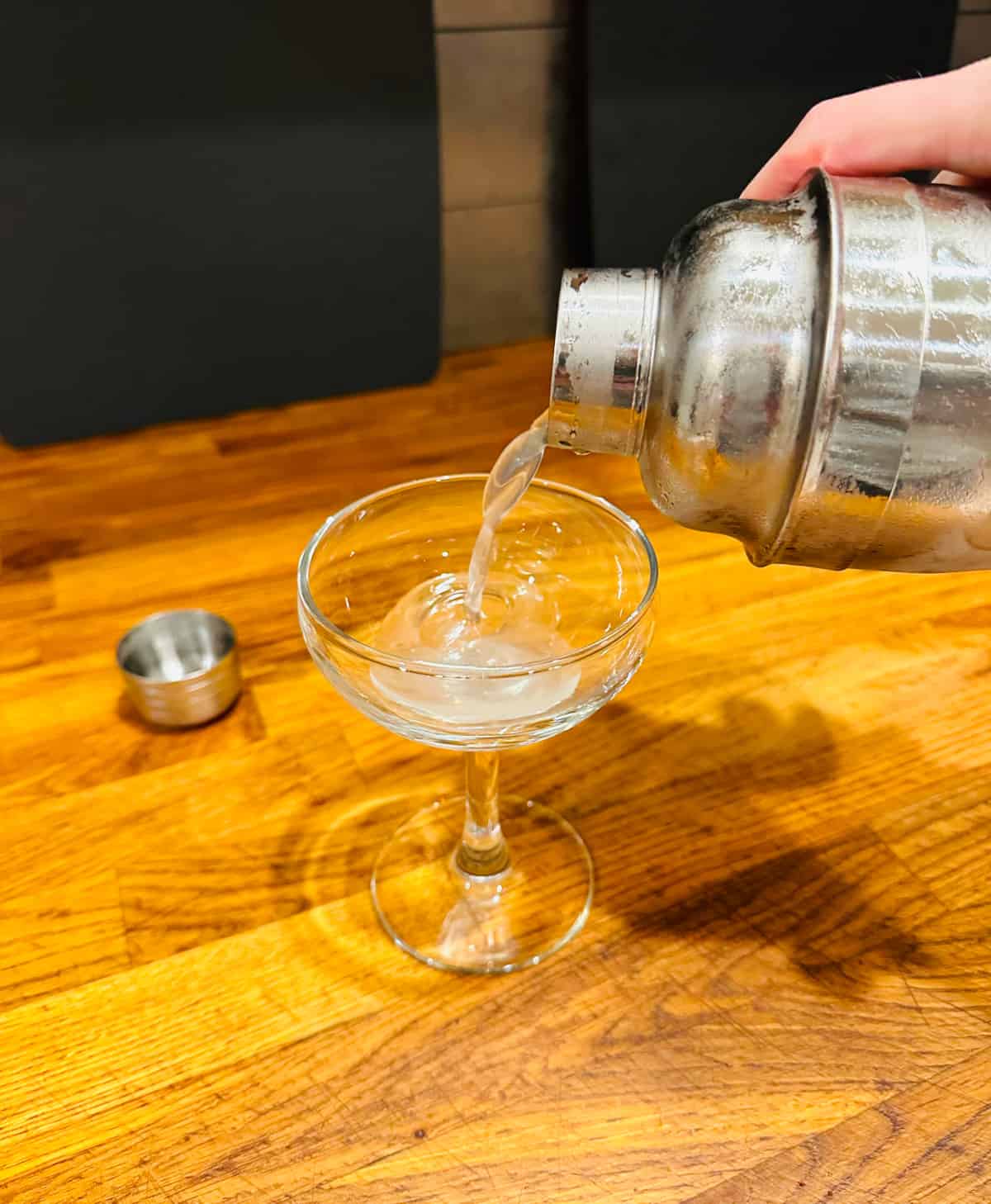 Ginger martini being poured from a cocktail shaker into a coupe glass.