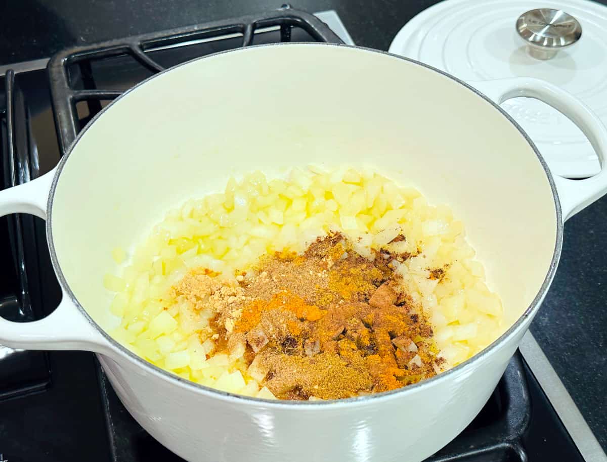 Spices sprinkled over cooked onions in a large white pot on the stove.