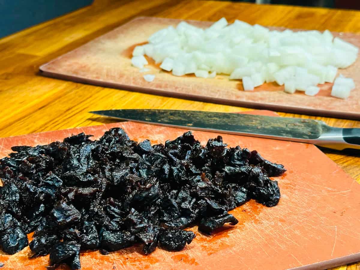 Chopped prunes and chopped onions with a chef's knife in between.