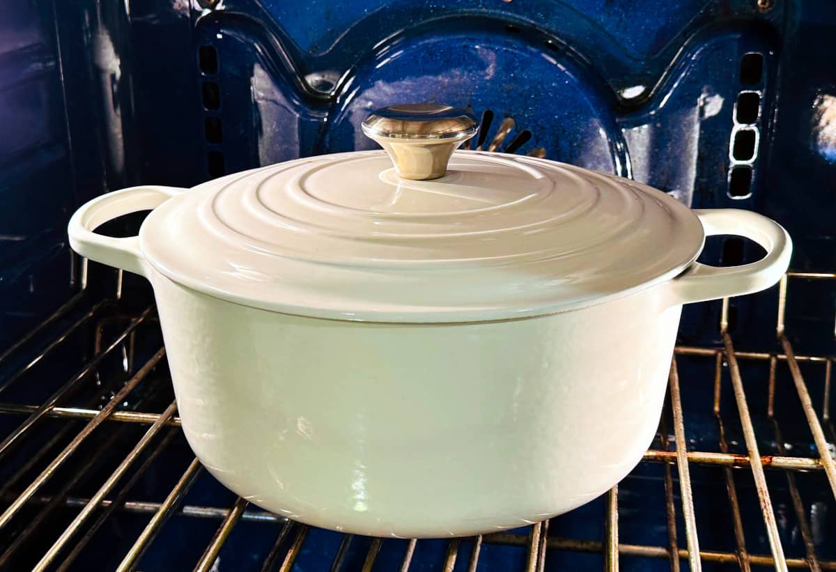 A large white pot covered with a lid sitting in a blue oven.