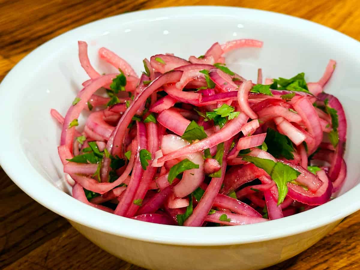Red onion topping flecked with chopped cilantro in a white bowl.