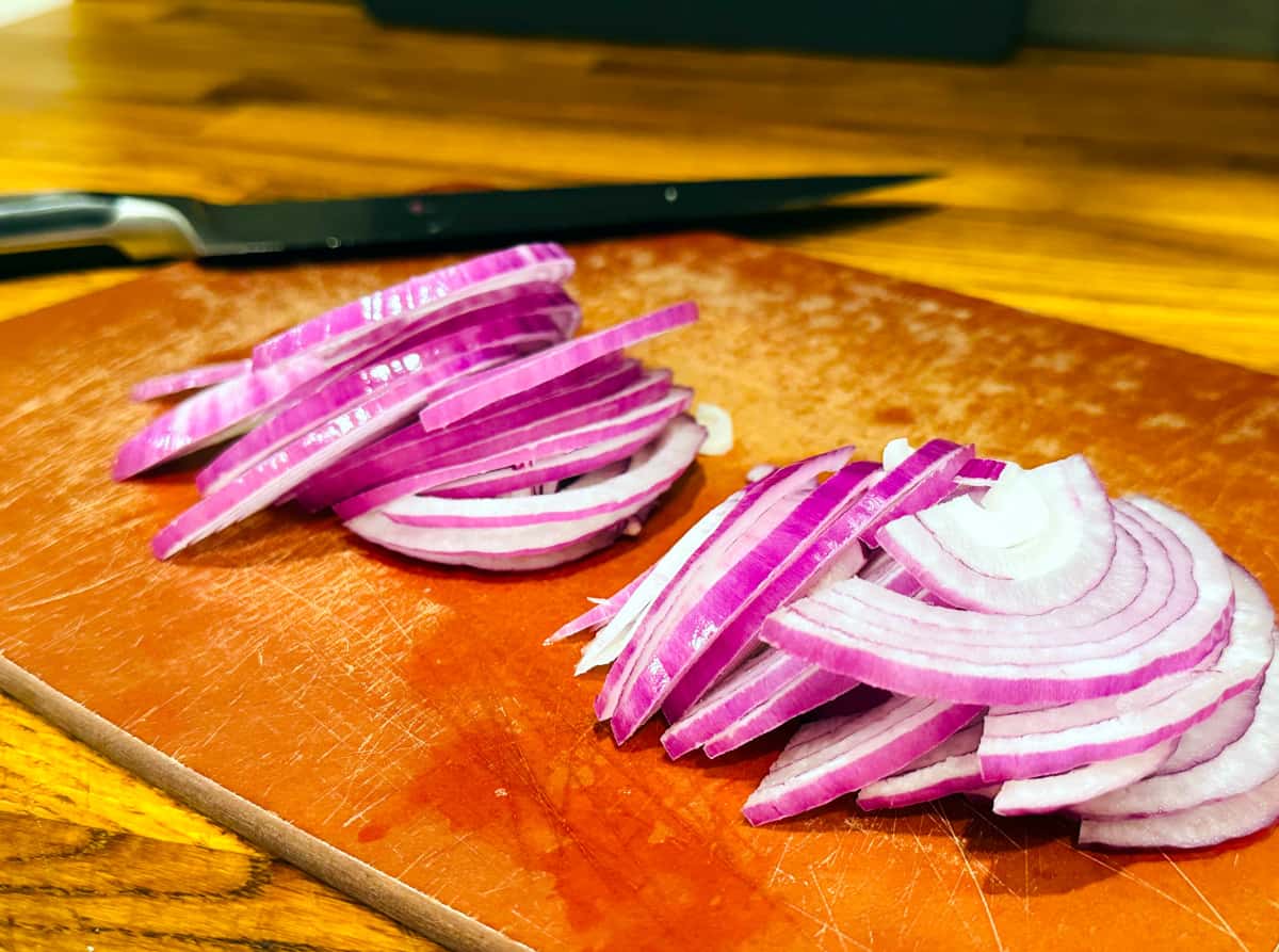 Red onions sliced into half moons next to a chef's knife.