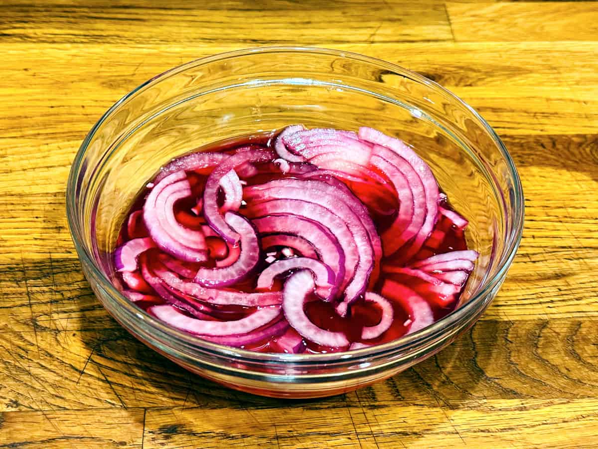 Red onions being steeped in pomegranate juice in a glass bowl.