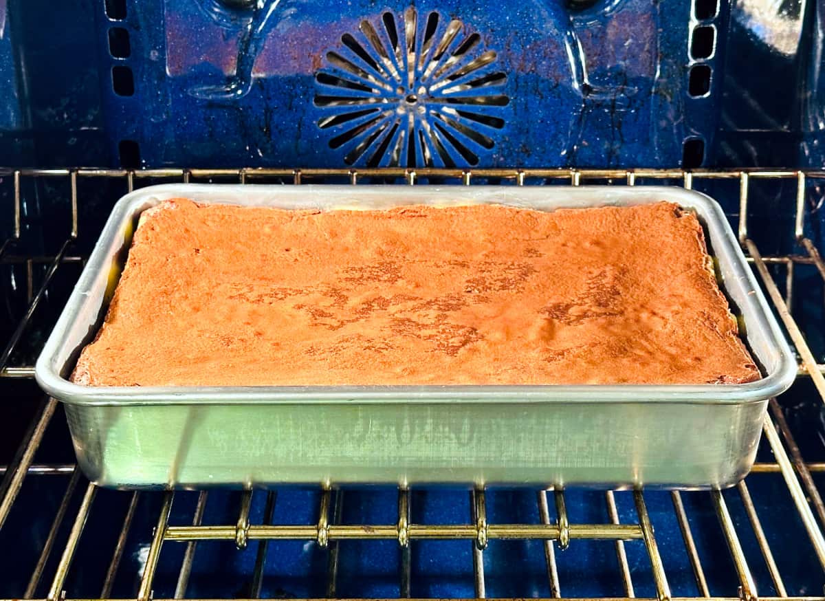 Peppermint cream cheese brownies in a metal baking pan baking in a blue oven.