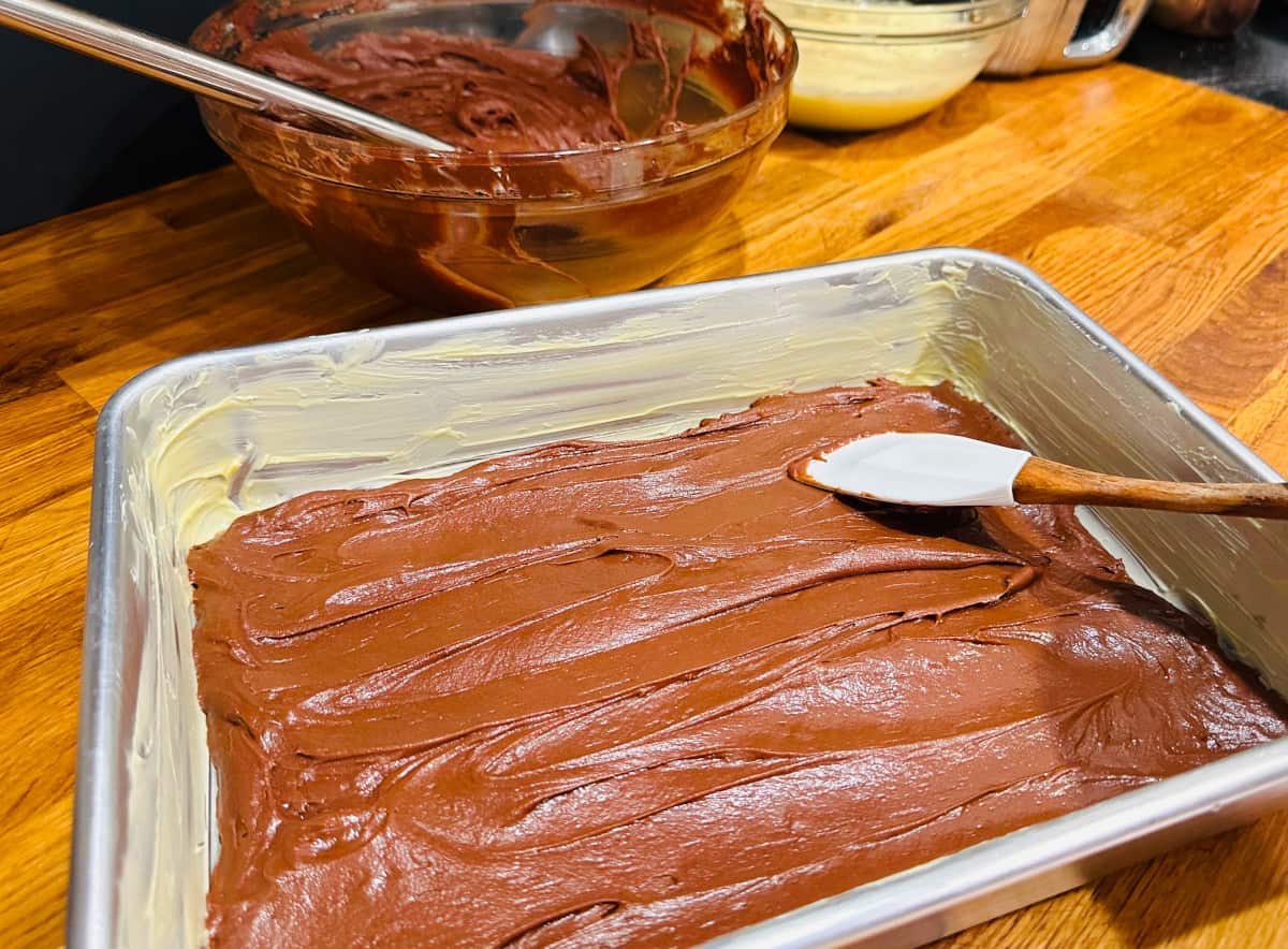Chocolate batter being spread by a silicone spatula in the bottom of a greased baking pan