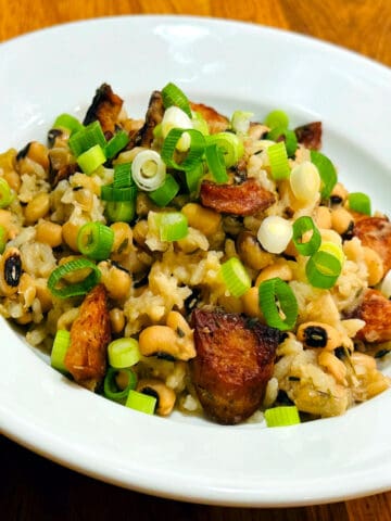 Hoppin' John garnished with chopped scallions in a shallow white bowl.