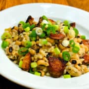 Hoppin' John garnished with chopped scallions in a shallow white bowl.