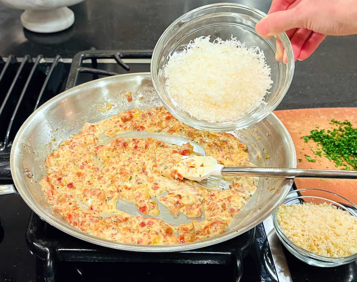 Grated white cheese being tipped from a small glass bowl into a mixture of cooked pancetta, shallot, sage, and mascarpone in a large steel skillet.