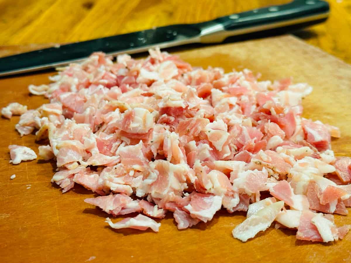 Chopped pancetta and a chef's knife on a brown cutting board.