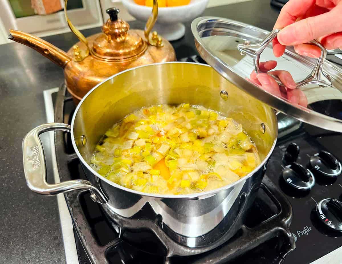 Lid being placed broth and vegetables simmering in a steel pot.