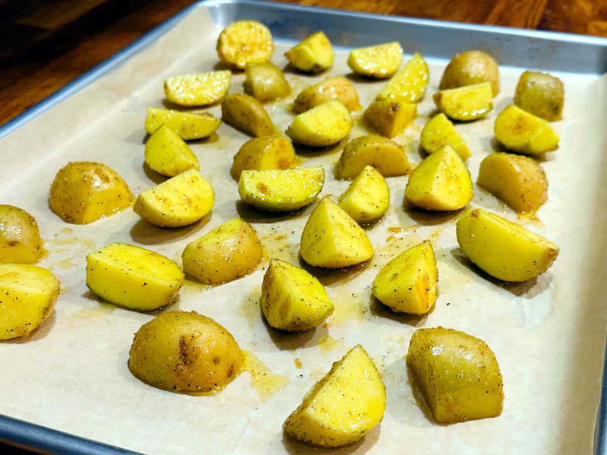 Quartered yellow potatoes coated in olive oil and seasonings spread out on a metal baking sheet lined with parchment paper.