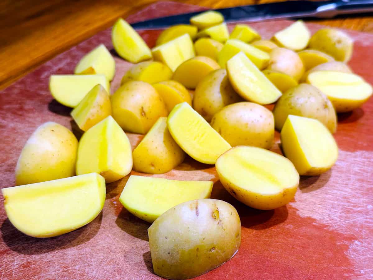 Quartered yellow potatoes on a brown cutting board.