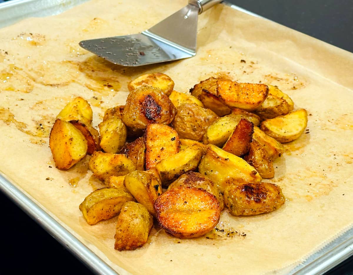 Roasted breakfast potatoes piled together on a parchment lined baking sheet next to a small metal spatula.