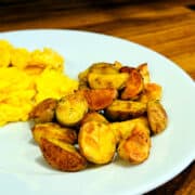 Breakfast potatoes on a white plate with some scrambled eggs alongside.